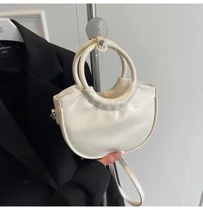 Detail of white semi-circular handbag with round metal handle and glossy finish