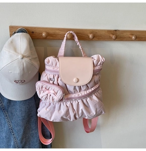 Detailed view of pink nylon backpack with ruffle design and small bow charm on a hook