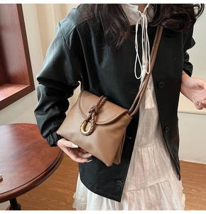 Detail of caramel leather envelope bag with woven strap and gold horseshoe buckle