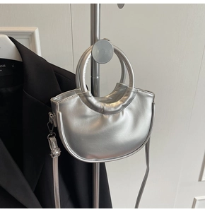 Close-up of silver crescent handbag with metallic handle on a minimalist background
