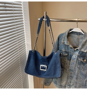 Detailed shot of dark blue denim shoulder bag with silver buckle and metal chain strap