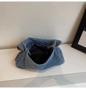 Detail of blue denim shoulder bag showing interior lining, pocket and silver chain strap