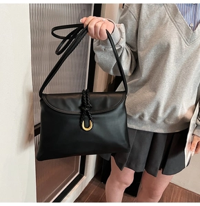 Detail of black leather bag featuring a woven knot design and U-shaped gold hardware