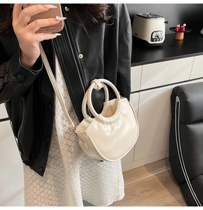 Detail of cream white half-moon crossbody bag featuring double ring handles and leather texture