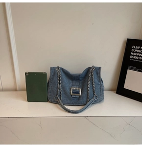 Detail of blue denim shoulder bag with silver square metal buckle and chain strap