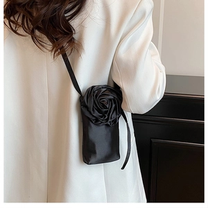Detail einer schwarzen Satin-Handytasche mit großer 3D-Rose auf weißem Blazer