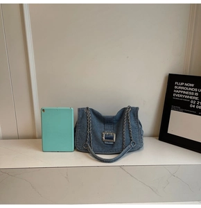 Detail of denim shoulder bag with metal buckle and chain strap next to a tablet for size