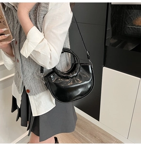 Detail view of glossy black bucket bag showing its curved shape and round handle