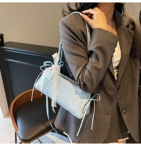 Detail of light blue shoulder bag with white lace bow and ribbons on leather surface