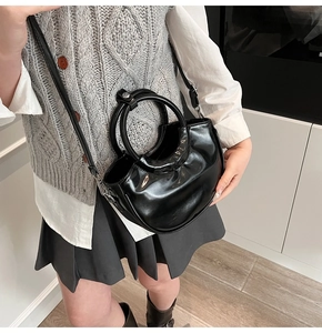 Model wearing a black glossy crescent handbag with round handle and leather strap