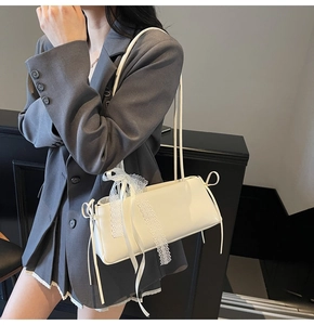 Close-up of a white leather baguette bag featuring a decorative lace bow on the side