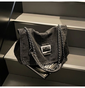 Detail of vintage denim bag with large silver metal buckle and chain strap on grey steps