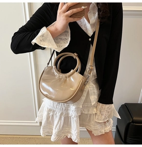 Polished khaki leather handbag with ring handles and shoulder strap shown on model