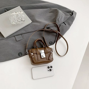 Mini sac bandoulière marron en cuir avec boucles argentées sur bureau minimaliste