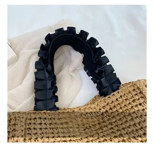 Detail of handmade straw tote bag with black pleated fabric handles and woven texture