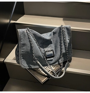 Detail of blue denim shoulder bag with chain strap and black square buckle on stairs