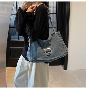 Detail view of denim shoulder bag featuring silver buckle and metal chain strap on model