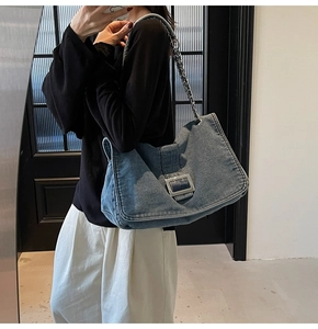 Detail of blue denim tote bag featuring a chunky silver chain strap and large metal buckle