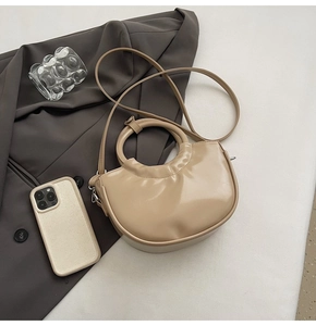 Detail of elegant beige semi-circle handbag with smooth patent leather and round handle