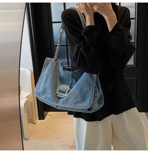Detail of blue denim tote bag featuring a large silver buckle and metal chain strap
