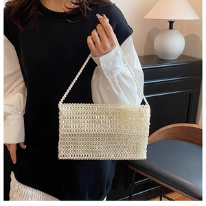 Detail of a handmade white pearl beaded handbag with an elegant woven handle on a model