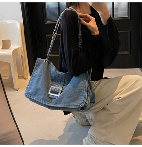 Detail of blue denim tote bag with silver metal buckle and chain strap on model