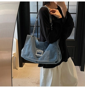 Detailed shot of large denim tote bag featuring oversized silver metal buckle and chain strap