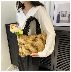 Detailed texture of handmade straw tote bag with black pleated handles and floral decor