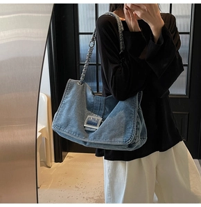 Close-up of blue washed denim tote bag featuring a silver square buckle and chain strap