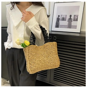 Detail of hand-woven straw tote bag with black pleated handle and french floral accent