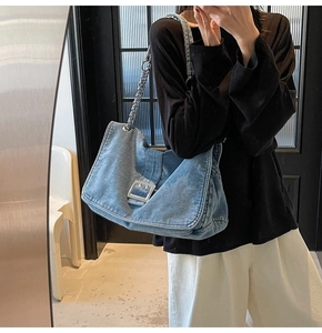 Detail of blue denim tote bag featuring silver chain strap and metal buckle closure
