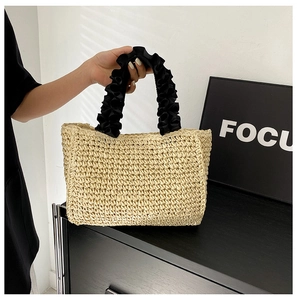Detailed close-up of woven straw tote bag with black ruffled satin handles for summer beach