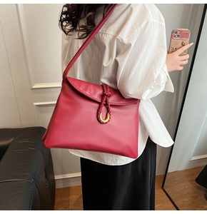 Detail of red leather shoulder bag featuring a braided knot and gold U-shaped metal clasp