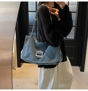 Detail of blue denim tote bag with silver metal buckle and chain strap shown on shoulder
