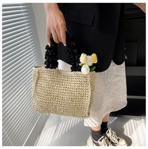 Detail of a handmade straw tote bag with black pleated fabric handles and tulip flowers