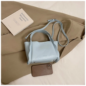 Close-up of light blue pebbled leather bucket bag with metal studs and logo detail