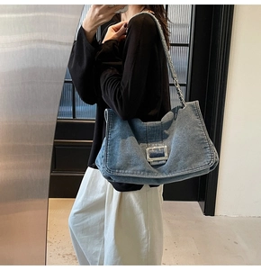 Detail of blue denim tote bag with large silver metal buckle and chain shoulder strap