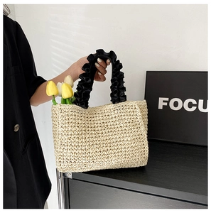 Detail of handmade straw tote bag with oversized black ruffled handles for beach vacations