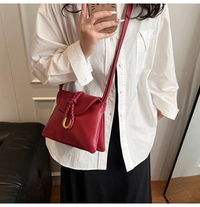 Detail of red leather crossbody bag featuring woven rope accent and golden U-shaped buckle
