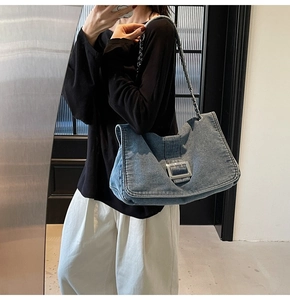 Detail of blue denim tote bag with large square metal buckle and chain leather strap