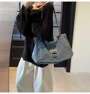 Detail of light blue denim tote bag with large silver buckle and metal chain strap