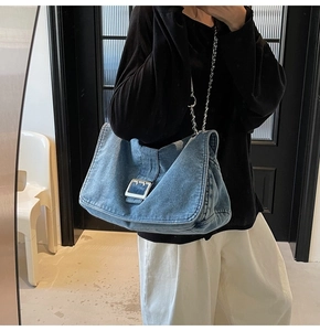 Detail of blue washed denim tote bag with silver metal buckle and chain shoulder strap