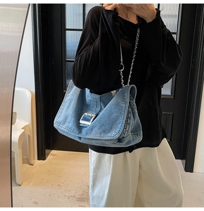 Detail of blue denim tote bag with large silver metal buckle and chain strap on shoulder