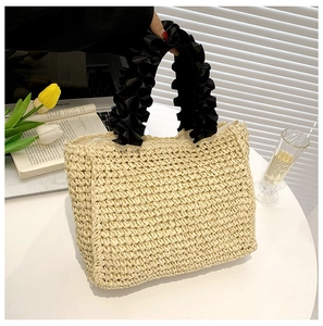 Detail of hand-woven straw tote with elegant black ruffled satin handles on a desk