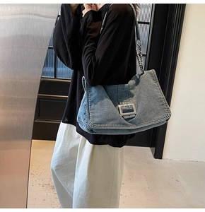Detail of blue denim tote bag featuring silver buckle and metal chain strap on model