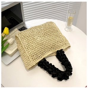 Detail of beige straw tote with black pleated satin handles on a leisure tabletop