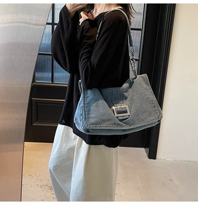 Detail of blue denim shoulder bag with silver buckle and chain strap on a model