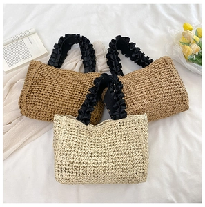 Overhead view of woven straw handbags with black ruffled handles on white fabric