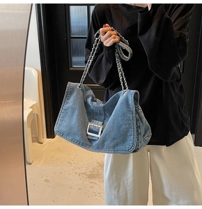 Close-up of denim shoulder bag featuring silver metal chain and square buckle detail