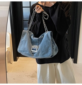 Close-up of blue denim shoulder bag with silver buckle detail and chain strap